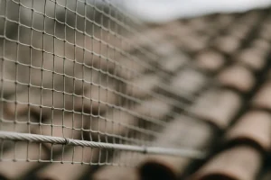 Dispositif anti-pigeons en maille métallique installé sur des tuiles de toit.